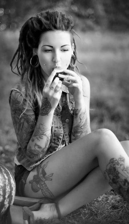 tattooed girl with dreadlocks eating on grass