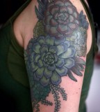 alice carrier tattoo blue and green coloured flowers on upper arm