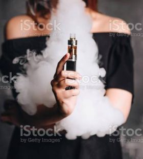 Close-up photo of female holding e-cigarette with smoke. Indoors