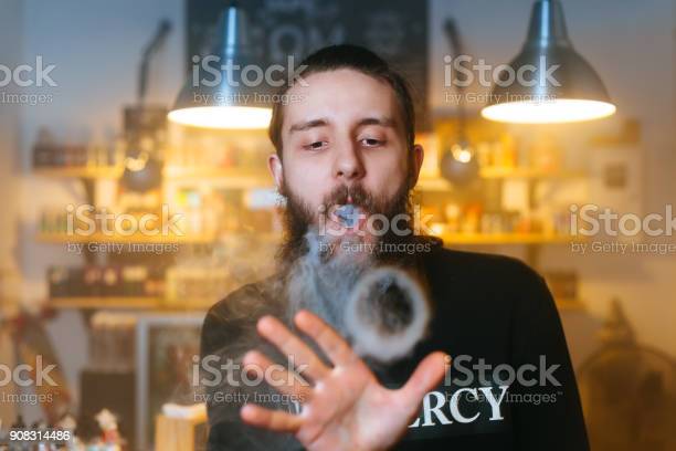 Men with beard vaping and releases a cloud of vapor.
