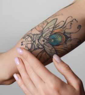 Woman,Applying,Cream,On,Her,Arm,With,Tattoos,Against,Light